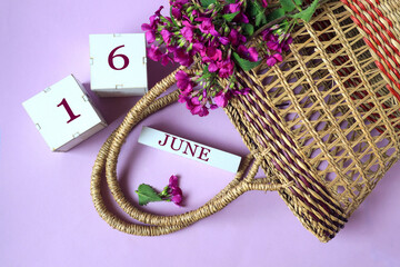 Calendar for June 16: cubes with the number 16 , the name of the month of June in English, a wicker basket and a bouquet of purple flowers, pastel background, top view