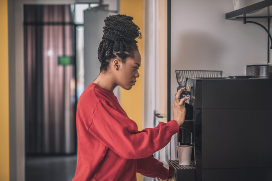 Dark-skinned young woman standing near the coffee-machine