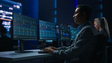 Confident Male Data Scientist Works on Personal Computer in Big Infrastructure Control Room. Stock Market Male Specialist Uses Computer Showing Charts, Information. Monitoring Room Team