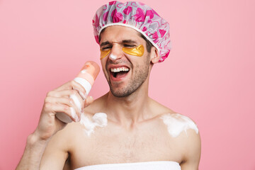 Young white man wearing shower cap holding shampoo and singing