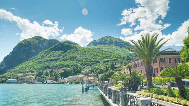 The famous coast of Menaggio, on Lake Como, Italy. On the right  the street leading to the village centre. On the left the waters of the lake. Alps, blue sky and clouds on the background. Timelapse.