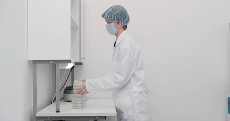 Female scientist in white coat, mask and cap working in lab