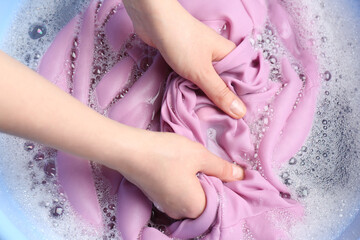 Top view of woman hand washing color clothing in suds, closeup