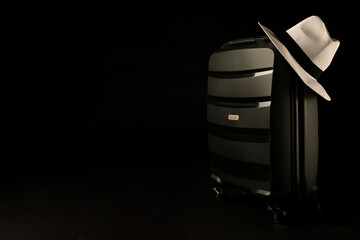 Holiday suitcase prepared with classic panama hat on black background, holiday concept, place for text.