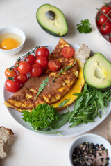 Omelette served with avocado, cherry tomatoes and arugula on ceramic plate. Healthy and tasty keto breakfast or brunch. Ketogenic diet. Top view.