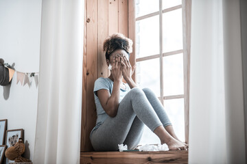 Woman covering face with hands sitting on windowsill