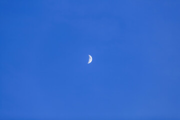 An incomplete disc of the moon in the form of a white crescent against a dark blue cloudless sky