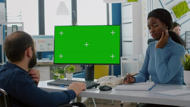 Diverse businessteam checking with financial graphs looking at green screen, mock up, chroma key izolated dysplay, black woman and paralysed coworker in wheelchair discussing solution for project