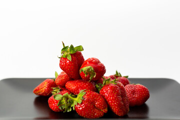 Red Strawberries a black plate. Natural fruits. White background.