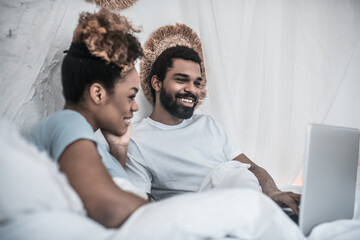 Cheerful man and woman looking at laptop in bedroom