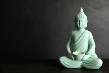 Buddha statue with burning candle on black table. Space for text