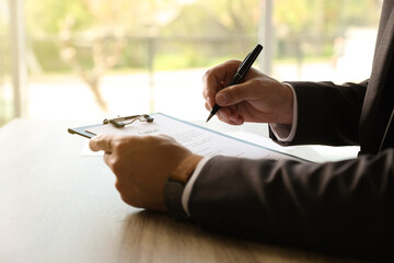 Businessman signing document at table indoors, closeup