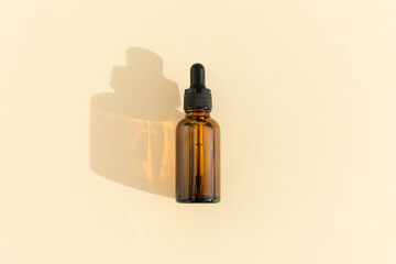 A glass bottle with a pipette for essential oil, lotion or serum on a pastel beige background. Dark amber glass bottle. Layout of the beauty salon branding