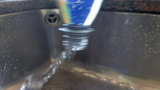 Close up shot of pouring fresh water from bottle into kitchen sink. Wasting water,save water,water conservation on planet. Slow motion.