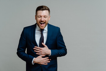 Excited businessman in suit keeping arms on stomach and having fun