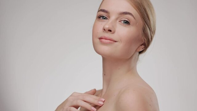 Slow-motion beauty portrait of young woman touching her smooth skin in collarbone area. Skincare concept. Female model with fresh skin smiling at the camera. Close up.