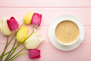 Cup of coffee with tulips on pink background