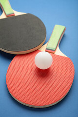 Ping pong rackets and ball on blue background with copy space. Vertical photo