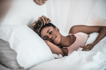 Dark skinned smiling woman napping in bed