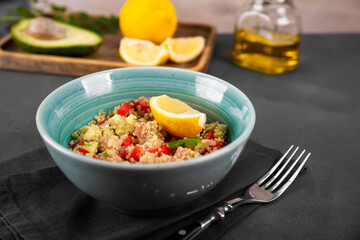  Salmon salad with tomatoes, avocado and quinoa in a blue bowl on a dark gray table, a dish of balanced diet