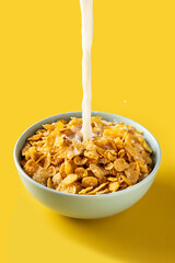 Pouring milk into bowl of corn flakes on yellow background