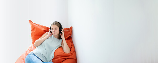 young woman relaxing on a bean bag pillow - female gen z with headphones listen to the music with closed eyes. banner with copy space with white background.
