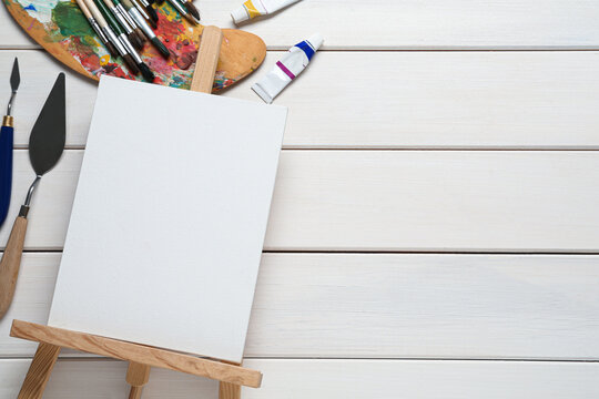 Blank canvas, tools and paints on white wooden table, flat lay. Space for text