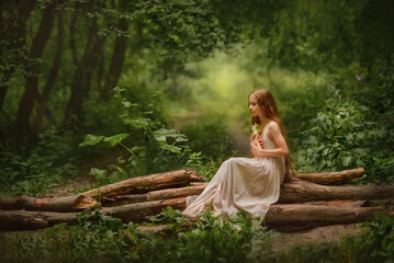 A girl with long hair with a flower in her hand sits on a log in the forest