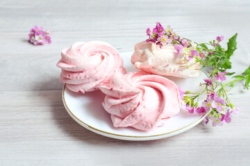 Three marshmallows lie on a plate with delicate pink flowers on a gray background, close-up