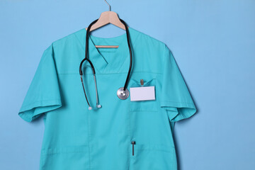 Turquoise doctor shirt with stethoscope and badge hanging on light blue background