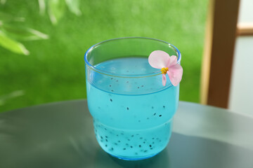 Tasty light blue drink with basil seeds on table