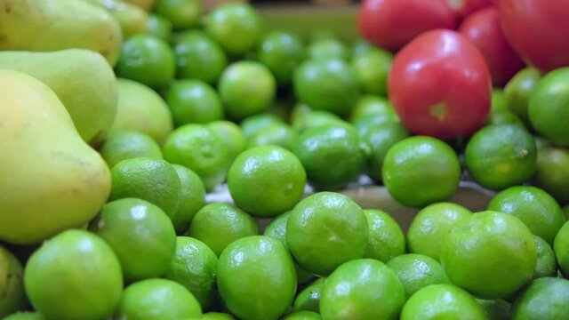 Close-up of fruit and vegetable stand with limes, mangoes, and tomatoes