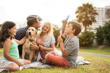 Young parents having fun with children and their pet outdoor at park in summer time doing picnic -...