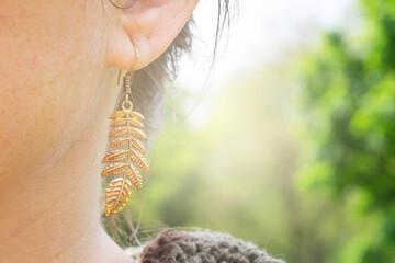 Outdoor detail of female ear wearing metal ornamental earring in natural shape