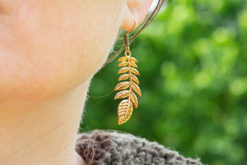 Outdoor detail of female ear wearing metal ornamental earring in natural shape