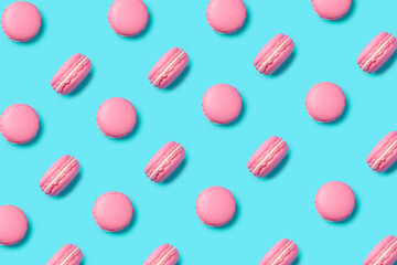 A row of pink macarons forming pattern on vibrant turquoise background. Creative food concept. Minimal patisserie or dessert composition. Flat lay, top view.