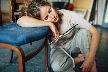 Horizontal image of an overworked female artist resting in her art studio. A tired woman painter falling asleep in her workshop place.