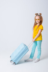 Portrait of a happy child of a girl in a yellow T-shirt on a white background with a suitcase. A studio shot of a cheerful kid with luggage.