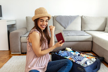 Shot of happy young woman preparing for big trip and vacation, she can not wait and have a fun with packing her props and clothes. Beautiful girl looking carefree and positive while packing her stuff.