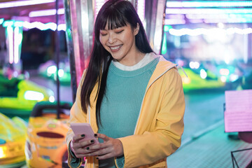 Happy asian girl using smartphone at amusement park - Focus on face