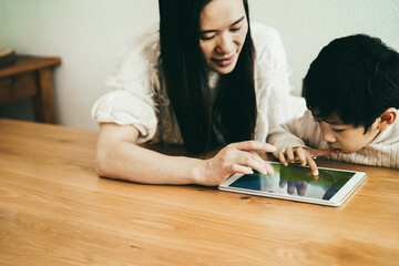 Asian mother and little son playing video games with tablet at indoors at home - Focus on boy face