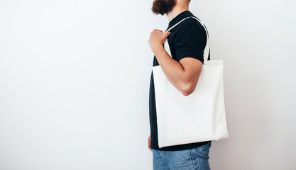 Young man is holding white textile eco bag on white background. Mockup for design