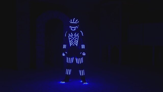 Man dressed in illuminated costume with colorful lights dancing and moving inside dark interior or club . Dancer guy wearing clothing with neon lights on his body and dances . Shot on ARRI camera .
