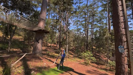 Slowmotion shot of a boy in a yellow helmet that is having fun in a rope climbing adventure park. Shot on a phone
