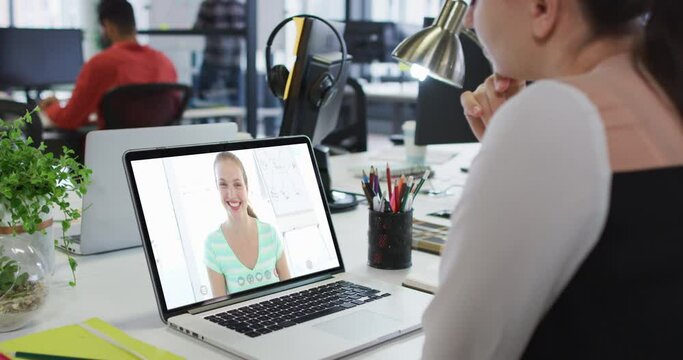 Caucasian woman having a video call with male and female office colleague on laptop at office