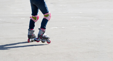 Children's feet on rollers ride on concrete, without face, view from the side, copying space, hard shadows