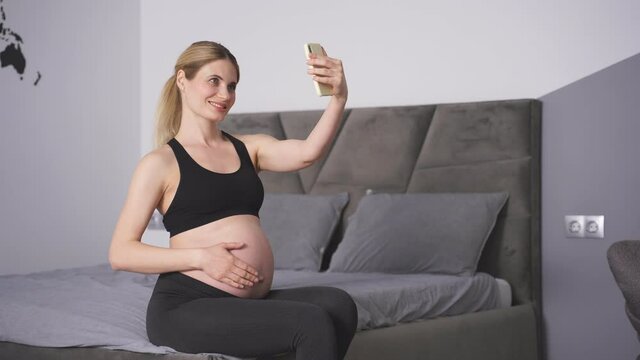 young Caucasian Pregnant woman Takes pictures of herself on her smartphone, Poses, smiles. The concept of pregnancy, technology, preparation and waiting for a child