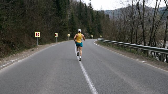A professional running athlete prepares for competitions and goes in for sports. A caucasian adult man runs past the camera in a special uniform with a T-shirt and shorts
