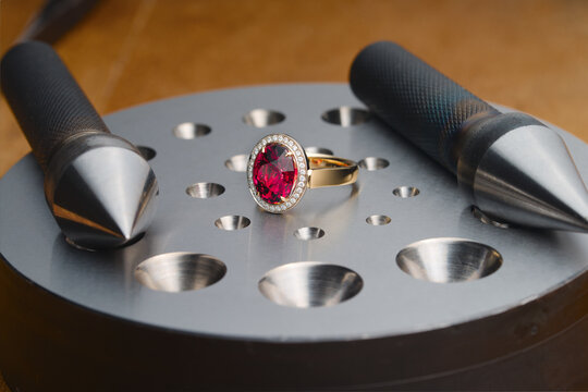 Luxury golden ring with ruby gemstone and bezel blocks on jeweler's desktop. Workplace of a jeweler. Tools and equipment for jewelry work on an antique wooden desktop.