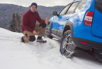 happy man with snow chains on car tire. winter scene in mountain landscape
